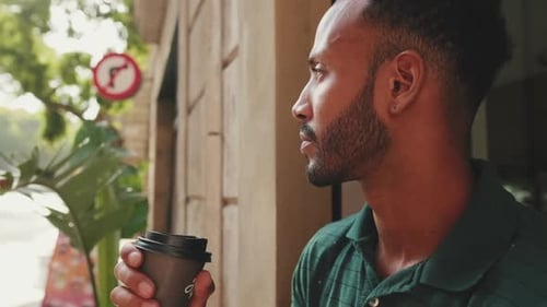 Close up, young man drinking coffee while sitting in street cafe on cityscape background