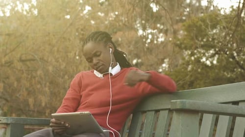 Man sitting on bench using tablet, listening to music