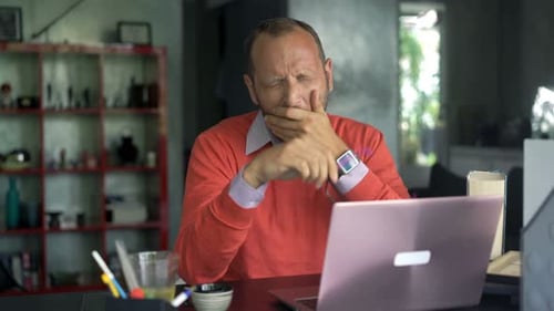 Tired man rubbing eyes while working at laptop
