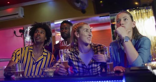 Video of diverse group of friends reacting to sports game on screen at a bar