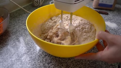 Bäcker mischt die Zutaten für Karottenkuchen in einer Schüssel mit dem Handmixer zum Backen. Nahaufnahme