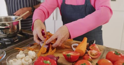 Mid section of diverse senior couple wearing aprons and cooking in kitchen