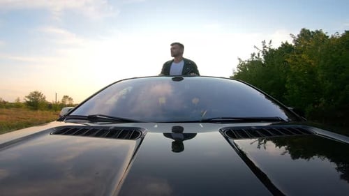 Front View of Young Man Standing Out of Car Sunroof and Showing Joyful Emotions During Road Trip