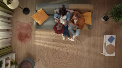 Top View of Living Room Mom Sitting on the Sofa Reading Smartphone Father and Son Come and Bring Her