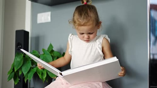 Girl Smiles While Looking at Picture Book Indoors