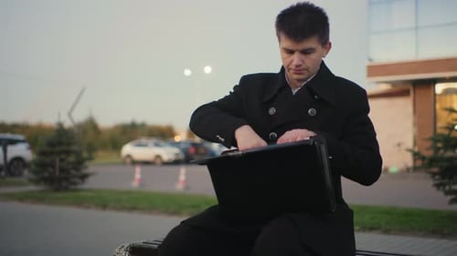 Young Adult Man Opens Briefcase on Bench