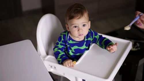 Adorable Baby Eating Food in Highchair Indoors