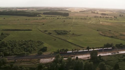 A train moving through the vast green countryside at dusk, aerial view