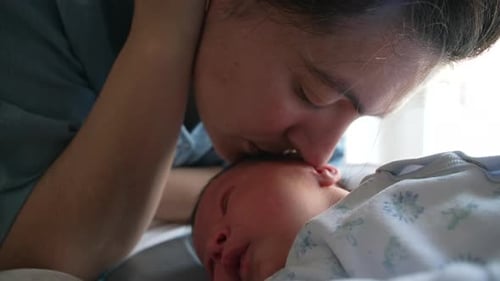 Loving Mother Kissing Newborn Infant at Home