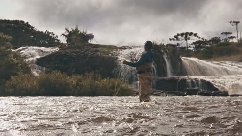 Man Fly Fishing in Flowing River Near Waterfall