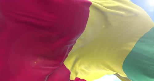 Realistic Waving Guinea Flag Against Blue Sky Background