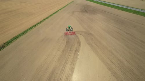 Aerial view of green double wheeled tractor with red cultivator preparing seedbed on agricultural fi