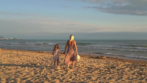 Mother and Daughter Walking on Sandy Beach at Sea at Sunset Summer Vacation