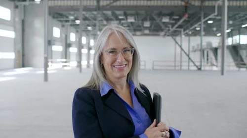 Smiling Woman Holding Laptop in an Empty Warehouse
