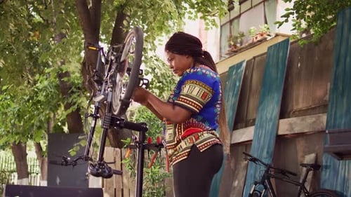 Woman Repairing Bicycle Outdoors on a Sunny Day