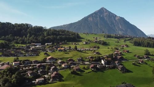 Aerial drone view of houses in village on green landscape by majestic mountain
