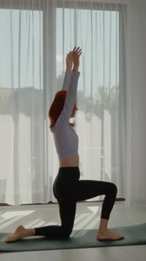 Vidéo verticale Une jeune rousse pratique le yoga dans un salon lumineux au lever du soleil