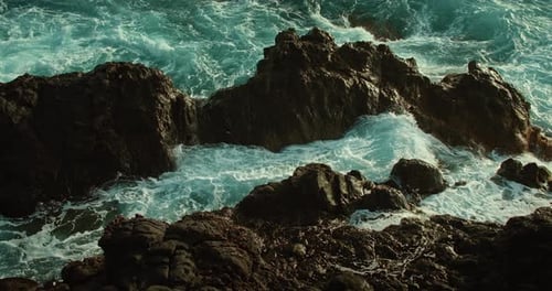 Ocean waves wash over rocky shore. Raging sea turquoise water foaming and splashing close-up cinemat