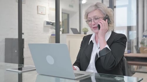 Senior Woman Working and Talking on Smartphone in Office