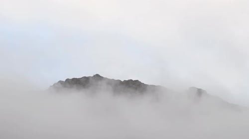 Fast moving clouds overcast the mountain. Clouds rolling over the mountain ridge
