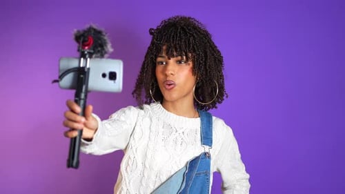 Young woman vlogger recording a video blog on purple background