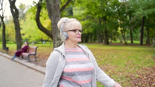 Portrait active senior woman walking exercise an alley a park or forest in nature and listening