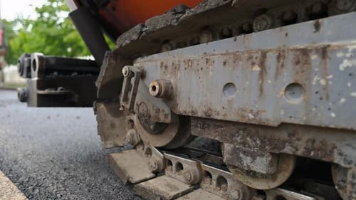 Asphalt tracked paver slowly moving on freshly made road - close-up. Special industrial vehicle