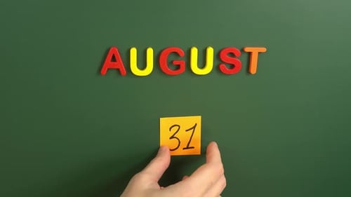 Hand sticking a sticker 31 August calendar day on school board. 31 date of august. Thirty first