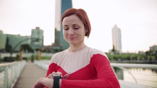 Young woman uses smartwatch while walking on a bridge in the city