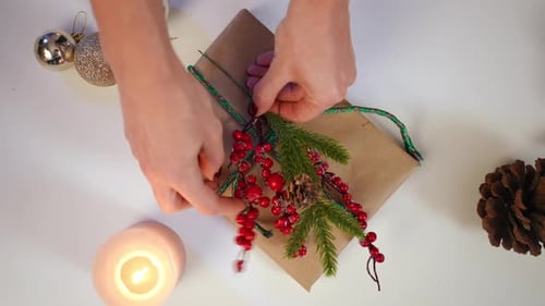 Top View Female Hands Decorating Christmas Present with Snowy Red Berries and Green Fir Branch with