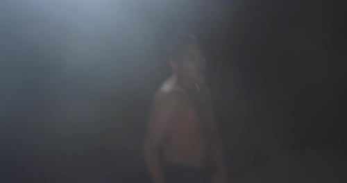 Der Junge führt professionellen Balletttanz mit Kurven in viel Rauch und gegen das Licht auf.