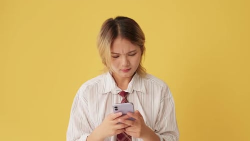 Upset woman using mobile phone, receiving bad news isolated on yellow background in studio