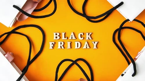 Zoom in Out Wooden Letters Text BLACK FRIDAY with Packaging Bags in Front Yellow Background Top View