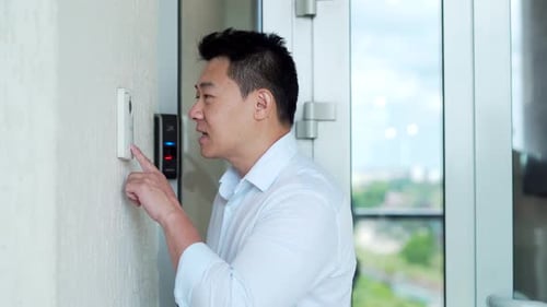Man Pushing Button on Intercom in Modern Building