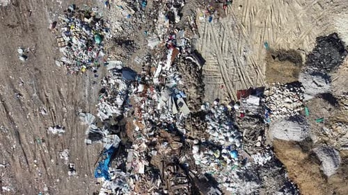 Aerial dump site with mixed household waste and visible tire tracks
