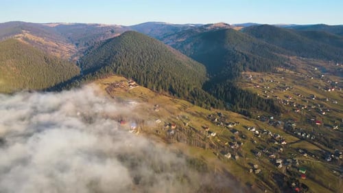 View From Above of Vibrant Landscape of Foggy Clouds Covering Mountain Hills and Village Houses at