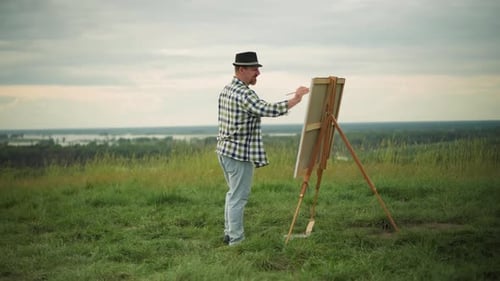 Artist Forcefully Painting on a Large Canvas in a Serene Field