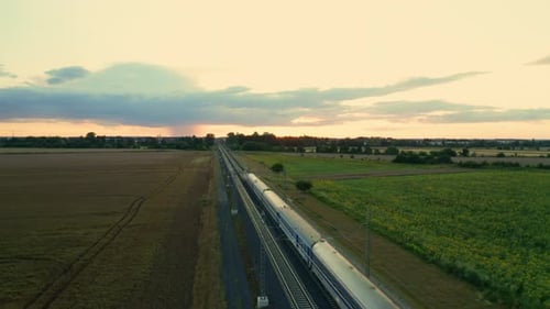Blue Passenger Train Passes Across Fields After Sunset at Twilight