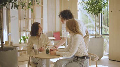 Two Women Conversing as Waiter Serves Drinks