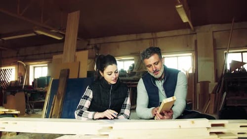Man And Woman Workers In The Carpentry Workshop, Making Plans.