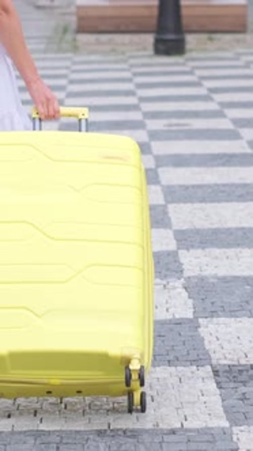 Woman Pulling Rolling Yellow Suitcase Along Paved Walkway