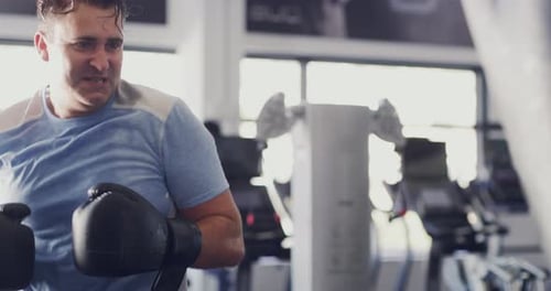 Active male athlete, sportsman and boxer boxing a punching bag at the gym, working on his routine