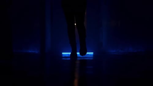Silhouette Woman Walks Along a Dark Corridor Shooting From a Low Point Blue Light