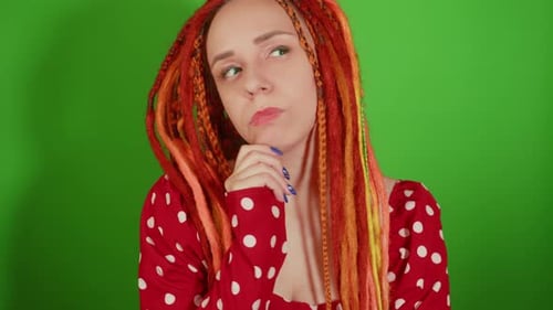 Thoughtful Young Woman with Dreadlocks Scratching Chin on Green Background