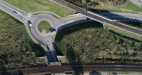 A traffic circle on a paved street with passing cars on a sunny day recorded from a drone in a wide