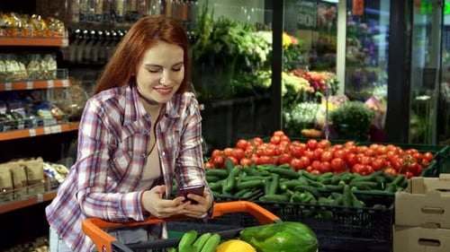 Cheerful Woman Checking Her Shopping List on a Smartphone in the Supermarket