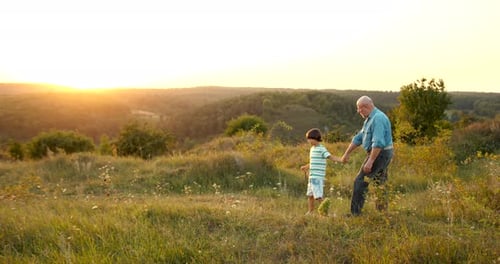 Grandfather and Grandson Walking at Sunset in the Field