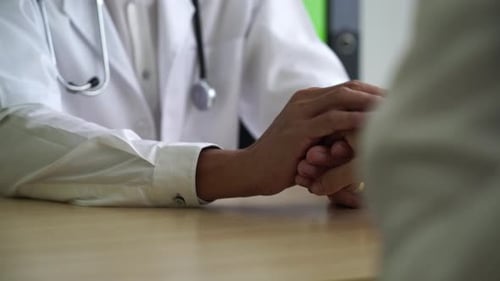 Doctor Comforts Patient by Holding Hands at Desk