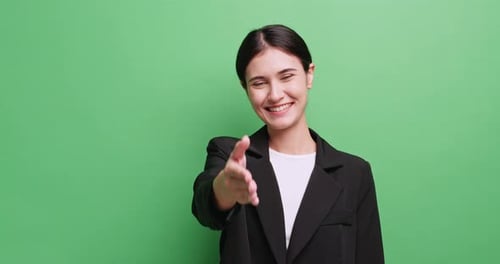 Young businesswoman makes a handshaking gesture. Isolated on green background in studio.