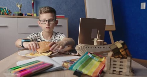 Boy Eating Burger While Using Laptop at Table